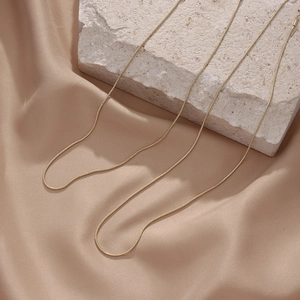 Detailed view of three gold snake bone necklaces draped over a stone and silk fabric