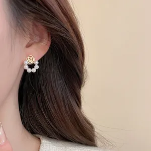 Close-up of elegant gold rose flower stud earrings with small pearls on a female model