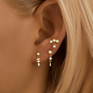 Close-up of gold cartilage studs featuring rhombus hollow flower design with green zircon