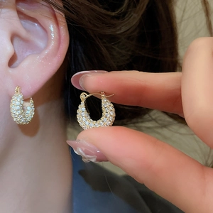 Macro shot of gold U-shaped hoop earrings paved with sparkling cubic zirconia crystals