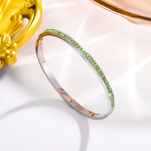 Detail of silver bangle featuring channel-set green square crystals on smooth silk fabric