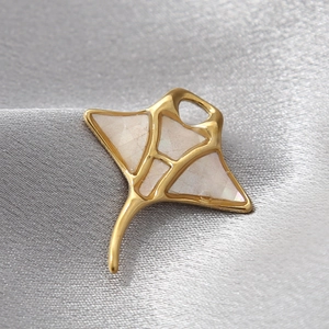 Macro shot of gold manta ray pendant with white shell inlay on a grey silk fabric