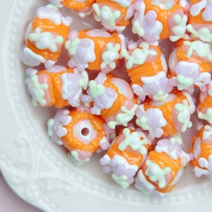 Macro view of orange handmade glass beads with floral patterns in a ceramic dish