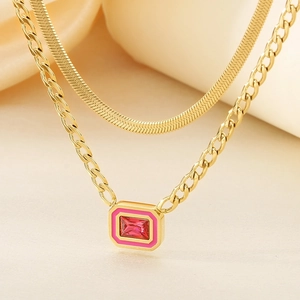 Macro detail of gold layered necklace featuring pink enamel and red crystal pendant
