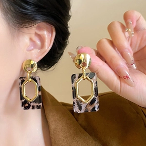 Close-up of leopard print acrylic earring with golden hexagonal metal details and studs