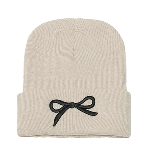 Détail du bonnet en maille épaisse avec un nœud noir brodé sur le rebord replié