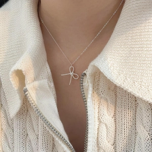 Detailed view of a silver bow necklace worn by a model on a beige knit sweater