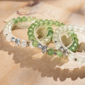 Macro detail of beaded bracelets featuring green chalcedony stone beads and silver fish charms