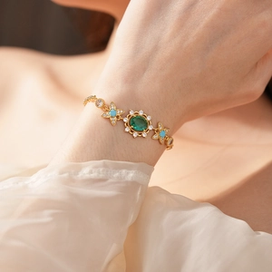 Détail d'un bracelet vintage doré avec pierre verte ovale et fleurs en zircone