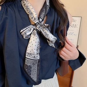 Detail of a black and white paisley silk scarf necklace tied in a bow on a female model