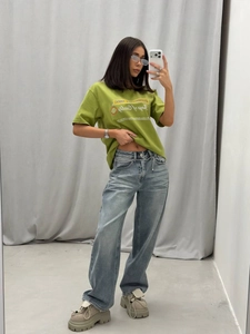 Selfie allo specchio con maglietta verde stampata e jeans dritti lavaggio blu