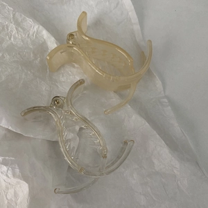 Close-up of minimalist transparent and beige fish-shaped hair clips on white paper