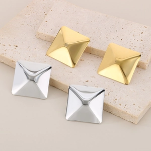 Close-up of gold and silver square pyramid earrings on a textured stone tray