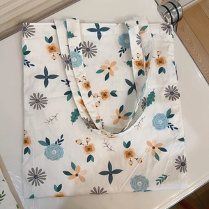 Detailed view of cream-colored floral canvas tote bag with blue rose and orange daisy prints