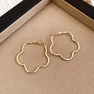 Close-up of artistic gold floral hoop earrings on a minimalist jewelry display tray