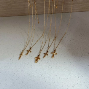 Set of five gold stainless steel necklaces with cross and dagger pendants on a wood beam