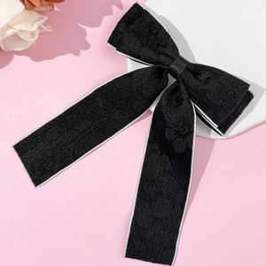 Detailed close-up of a black textured bow hair clip with white piping on pink background