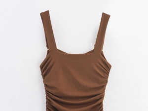 Detail of brown ruched dress with wide straps and metallic ring connectors on white background