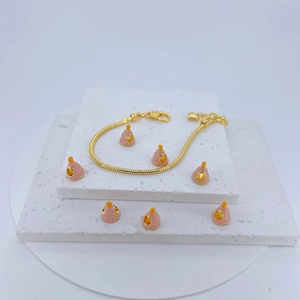 Gold snake chain bracelet featuring pink enamel charms on white stone display