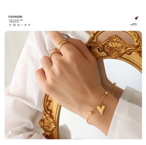 Detail of gold heart pendant bracelet and layered rings on French vintage frame background
