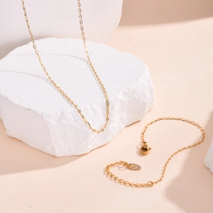 Close-up of gold chain jewelry detail with K18 engraving on a white stone background