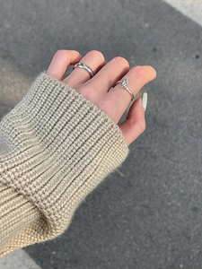 Dettaglio di un set di anelli d'argento a nodo abbinato a un maglione lavorato beige