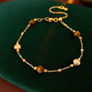 Close-up of gold-plated bracelet with brown tiger eye beads on green velvet background