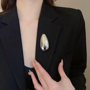 Close-up of polished silver teardrop brooch on a black suit blazer lapel