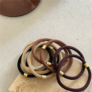 Elastic hair ties set in earth tones with gold metal accents on a textured stone surface