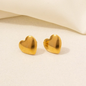 Detailed close-up of golden heart-shaped stainless steel stud earrings on soft fabric