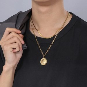 Close-up of a layered gold necklace featuring a snake chain and a religious medallion pendant