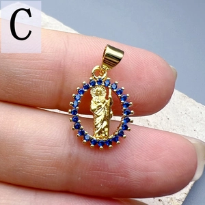 Detailed view of gold St. Jude pendant with blue cubic zirconia stones held in hand