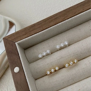 Detail of silver and gold stud earrings featuring three-stone zircon settings in a box