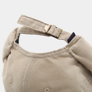 Detail of corduroy docker cap featuring an adjustable metal buckle and blue woven label