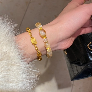 Detail of light yellow crystal bead bracelet and gold geometric chain worn by a model