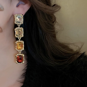 Close-up of long gold earrings featuring four geometric stones in champagne and amber