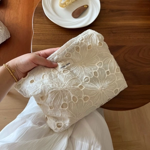 Detail of hand-held beige lace makeup bag with floral embroidery and simple wish tag