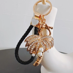 Golden coconut tree keychain with rhinestones, white pearls, and black braided leather strap