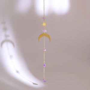 Detail of golden moon and sun charm with natural purple crystals on a hanging chain