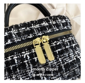 Close-up van gouden dubbele ritsen op een zwart-witte tweed schoudertas voor dames.
