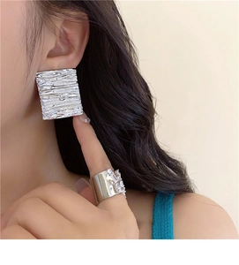 Detail of square silver textured earrings and wide zircon ring on a female model