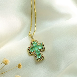 Detailed shot of golden cross necklace with green square zircon and silk background