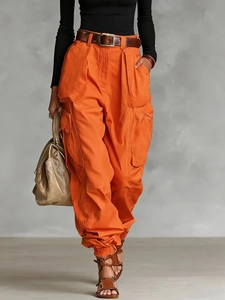 Detail of orange high-waisted cargo pants showing multi-pocket design and woven texture