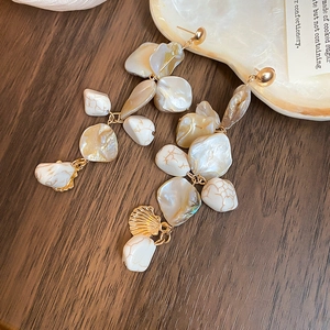Detailed top view of irregular shell tassel earrings with pearls on dark wood