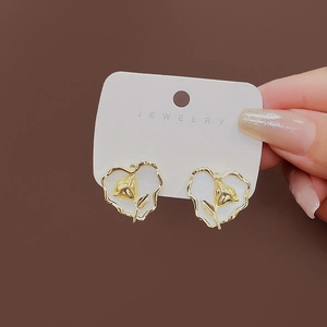 Detail of heart-shaped gold rose earrings with white resin inlay on a jewelry card