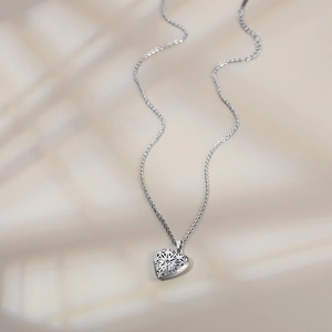 Detail view of silver heart locket necklace with intricate hollow pattern and crystal