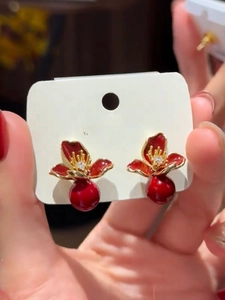 Détail de boucles d'oreilles fleurs rouges avec bords dorés et perle pendante brillante