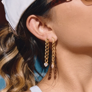 Gold chain drop earrings with heart and teardrop crystal pendants worn by a model