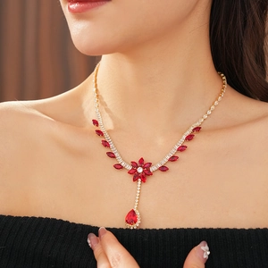 Close-up of elegant gold necklace with ruby red flower and teardrop pendants on model