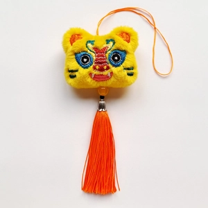 Détail du pendentif lion dansant en peluche jaune avec pompons orange et broderie